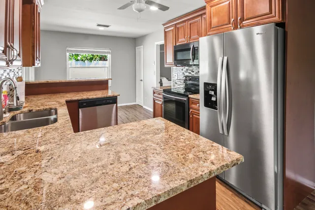 a kitchen with stainless steel appliances granite countertop a refrigerator a stove and a sink with wooden cabinets
