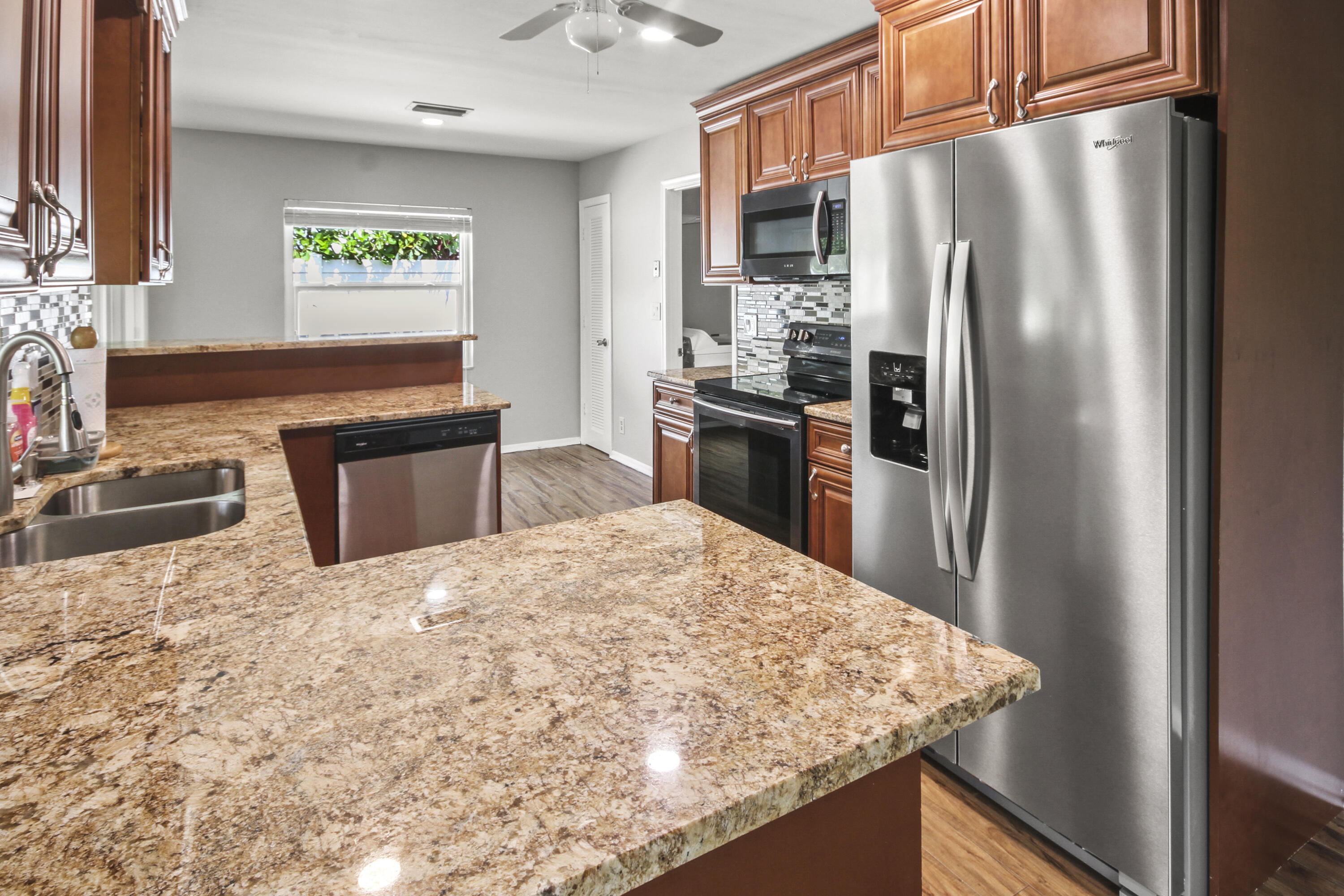 22493 Southwest 56th Avenue Boca Raton, FL 33433 - Photo 19 of 31 a kitchen with stainless steel appliances granite countertop a refrigerator a stove and a sink with wooden cabinets