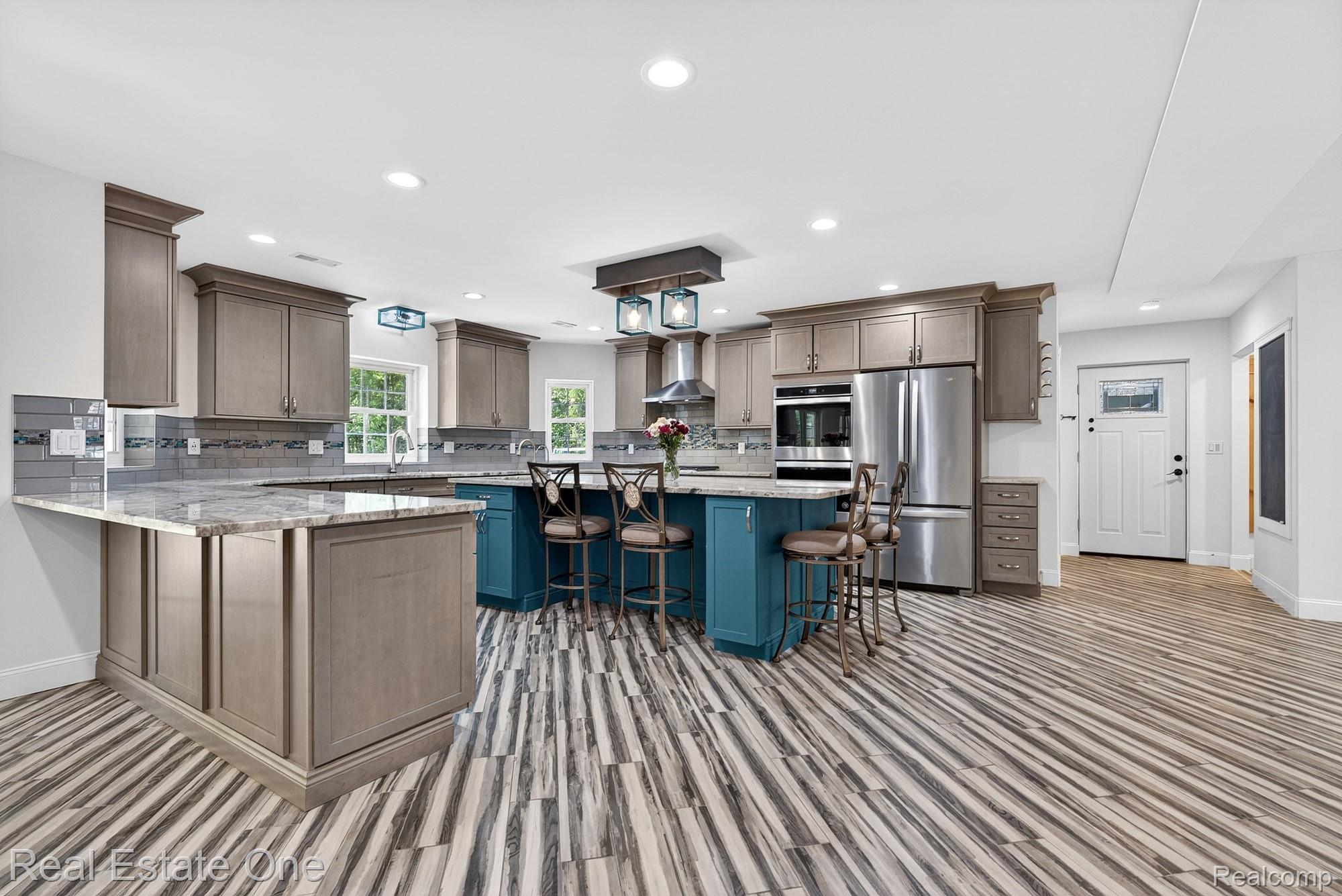 26987 Crawford Road Romulus, MI 48174 - Photo 8 of 51 Spacious kitchen featuring a large central island with seating, stainless steel appliances, extensive cabinetry, light-toned countertops, and wood-finish flooring