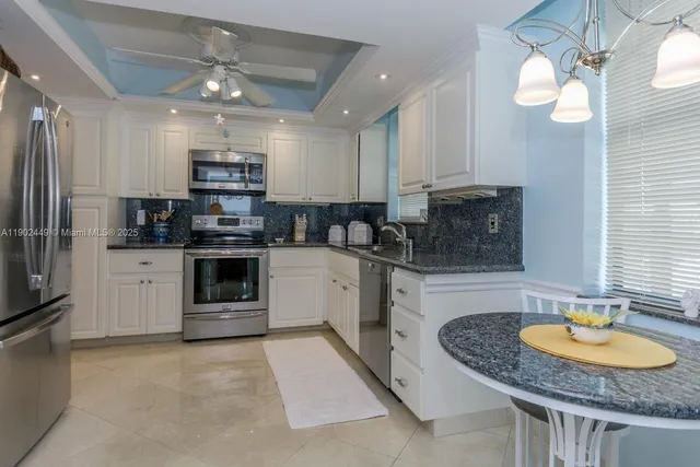 a kitchen with stainless steel appliances granite countertop a sink a stove a refrigerator cabinets and a dining table