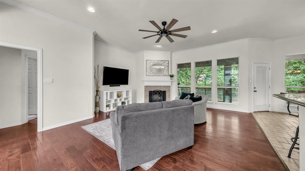 203 Mockingbird Lane Aledo, TX 76008 - Photo 10 of 37 Spacious living area featuring rich wood-finish flooring, a corner fireplace with a stone surround and white mantel, and a multi-blade ceiling fan