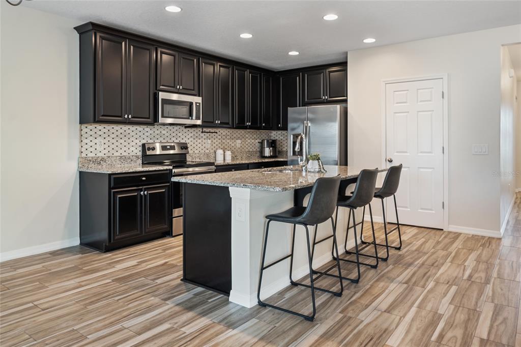 19041 Alfaro Loop Spring Hill, FL 34610 - Photo 4 of 39 a kitchen with stainless steel appliances granite countertop wooden cabinets a refrigerator a stove a sink and a microwave with wooden floor