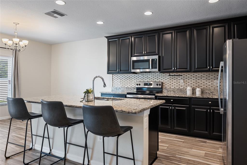 19041 Alfaro Loop Spring Hill, FL 34610 - Photo 7 of 39 a kitchen with stainless steel appliances granite countertop a stove top oven a sink dishwasher a dining table and chairs with wooden floor