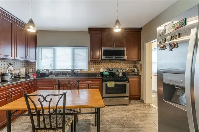a kitchen with stainless steel appliances granite countertop a stove top oven a refrigerator a sink and chairs