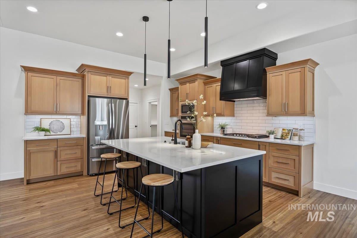 924 Trapper Peak Road Kimberly, ID 83341 - Photo 12 of 40 Kitchen with stainless steel appliances, a center island with sink, a kitchen bar, light stone countertops, and light wood-type flooring