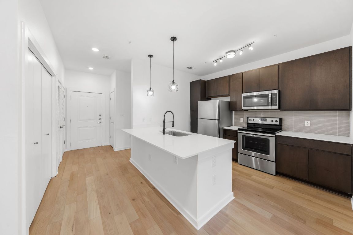 Kitchen with light wood finished floors, dark brown cabinets, appliances with stainless steel finishes, and a sink