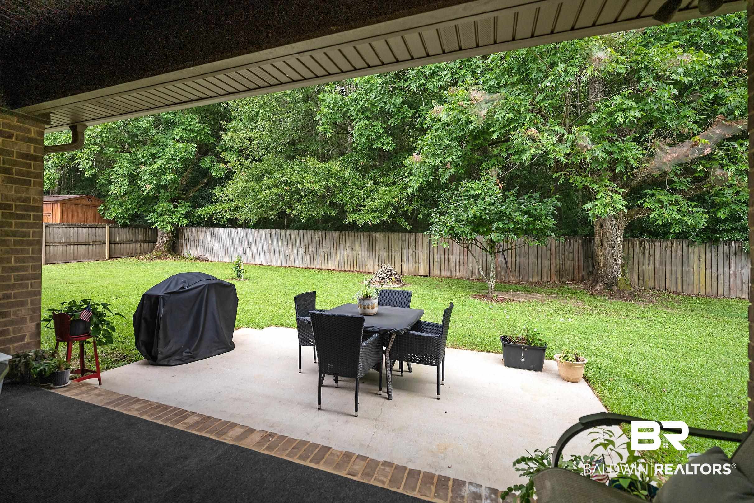 313 Pecan Ridge Boulevard Fairhope, AL 36532 - Photo 36 of 51 Covered concrete patio with a brick wall, bordered by a grass lawn and a wood privacy fence