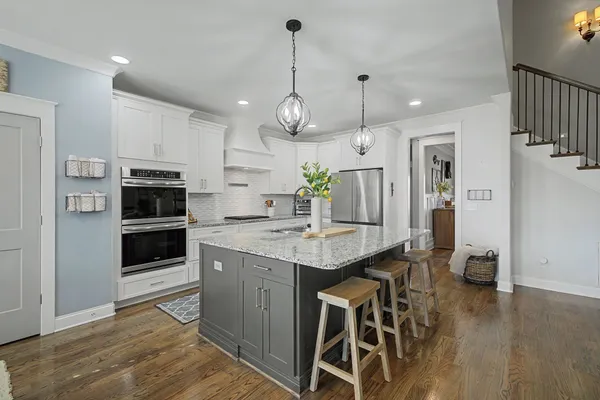 a kitchen with stainless steel appliances kitchen island granite countertop a table chairs and a wooden floors