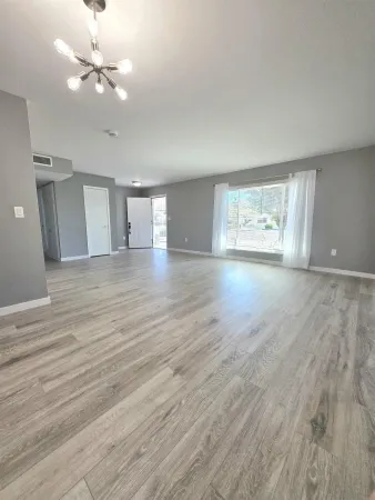 a view of an empty room with window and wooden floor