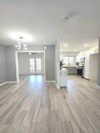 a view of an empty room and a kitchen with wooden floor