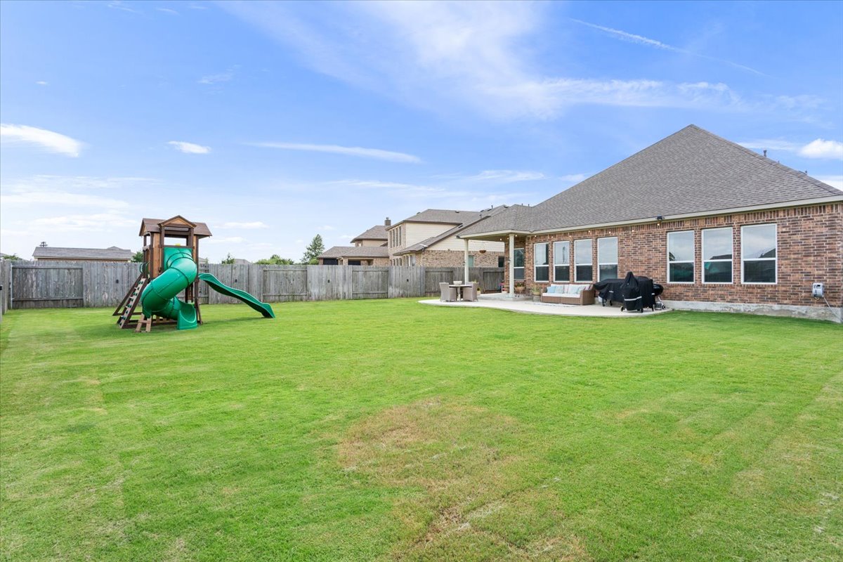 424 Millard Street Georgetown, TX 78628 - Photo 36 of 37 An expansive fenced backyard features a play set and covered patio for diverse outdoor enjoyment.