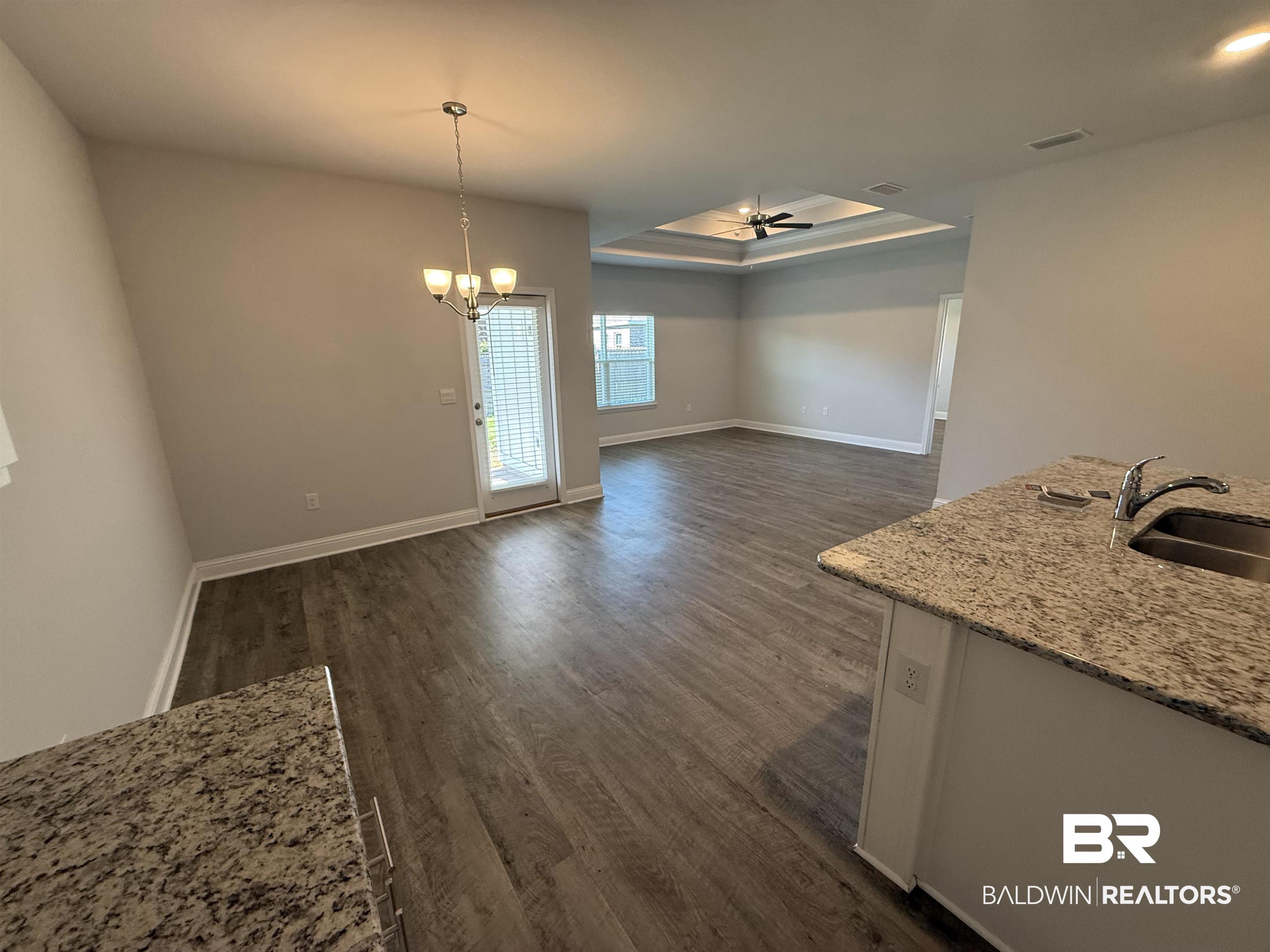 23247 Lieutenant Avenue Foley, AL 36535 - Photo 24 of 47 Open-concept interior featuring wood-finish flooring, a kitchen island with stone-finish countertop and undermount sink, a dining area with pendant lighting, and a living area with a tray ceiling and ceiling fan