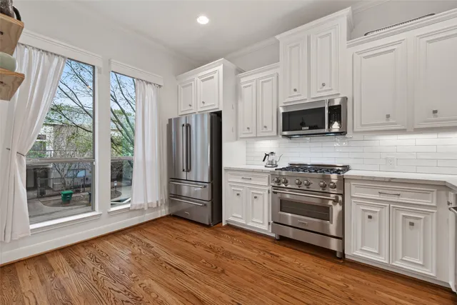 a kitchen with stainless steel appliances a stove a refrigerator a sink and white cabinets with wooden floor