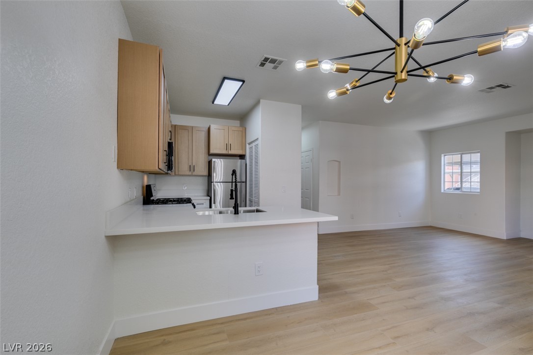 4730 East Craig Road, Unit 1085 Las Vegas, NV 89115 - Photo 5 of 23 A striking sputnik chandelier illuminates this open-concept living space, featuring a modern kitchen island and light wood flooring.