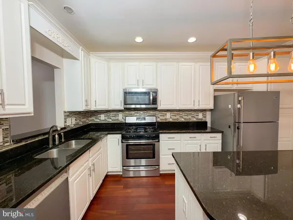a kitchen with granite countertop a sink a counter top space stainless steel appliances and cabinets