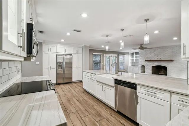 a large white kitchen with a stove a sink a refrigerator and white cabinets with wooden floor