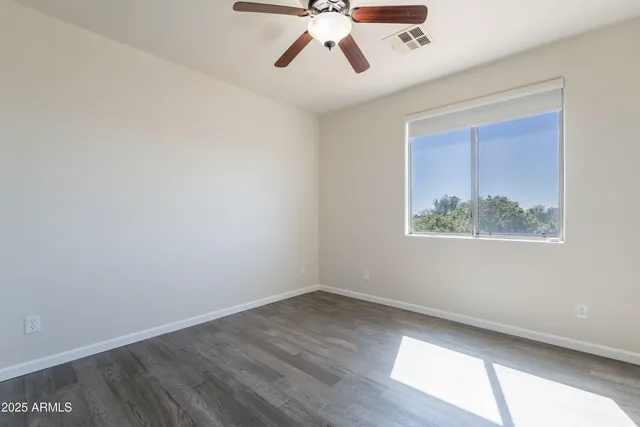 an empty room with wooden floor chandelier fan and windows