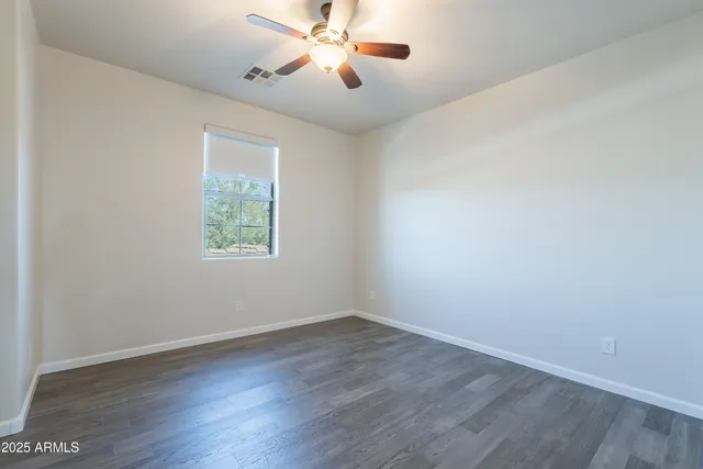 a view of an empty room with wooden floor and a ceiling fan