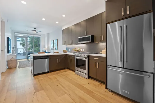 a kitchen with stainless steel appliances kitchen island granite countertop a refrigerator a sink dishwasher a stove and a refrigerator with wooden floor