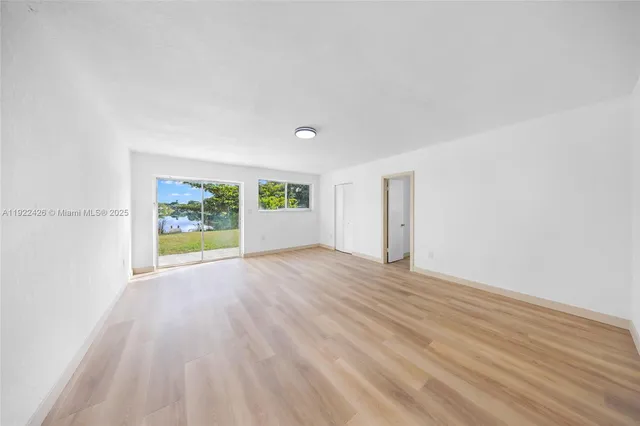 a view of an empty room with a window and wooden floor