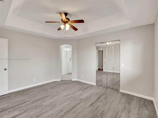 an empty room with wooden floor chandelier fan and windows