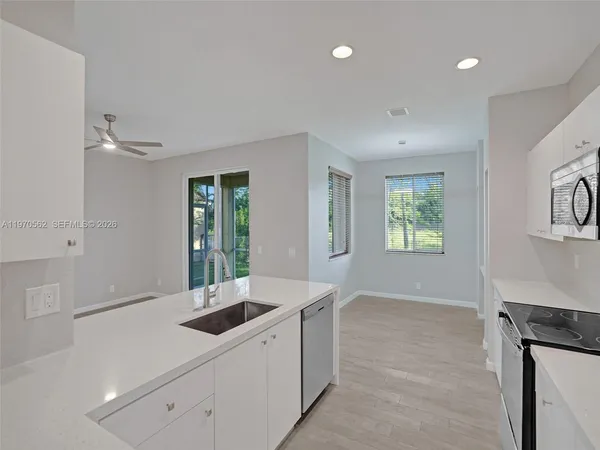 a kitchen with a sink dishwasher a stove and white cabinets with wooden floor