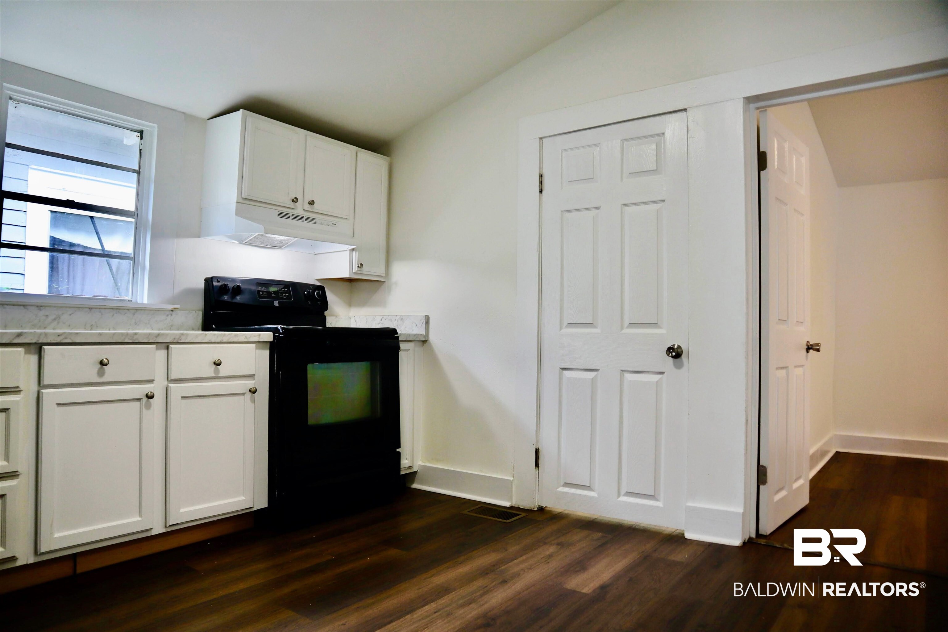 1009 Baltimore Street Mobile, AL 36605 - Photo 13 of 17 Kitchen with black range with electric cooktop, lofted ceiling, dark wood-style floors, white cabinets, and under cabinet range hood