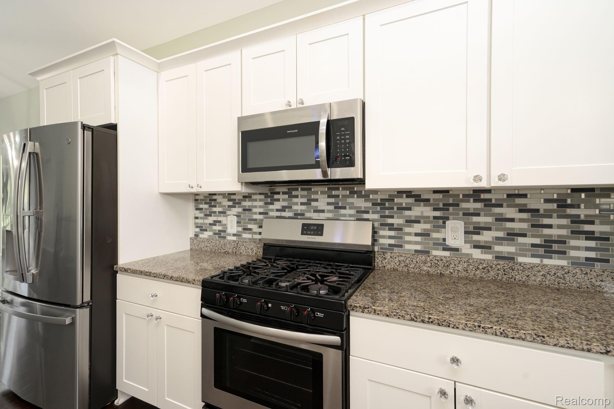 4610 East Clyde Road Howell, MI 48855 - Photo 18 of 54 Kitchen featuring stainless steel appliances, white cabinetry, a tiled backsplash, and stone countertops