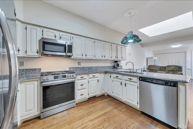 a kitchen with granite countertop a stove top oven a sink dishwasher and white cabinets with wooden floor