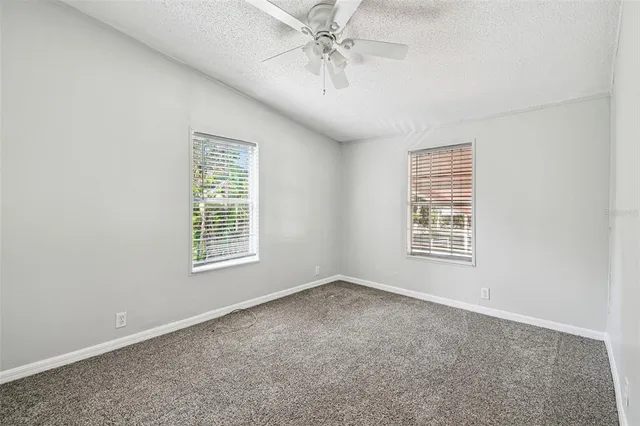 an empty room with chandelier fan and windows