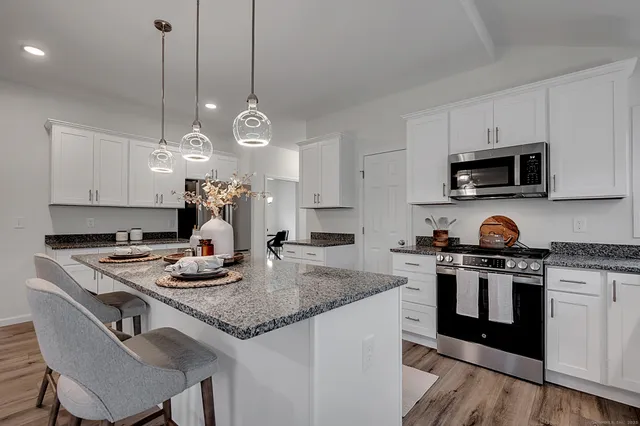 a kitchen with kitchen island granite countertop a sink a stove a microwave and wooden floor