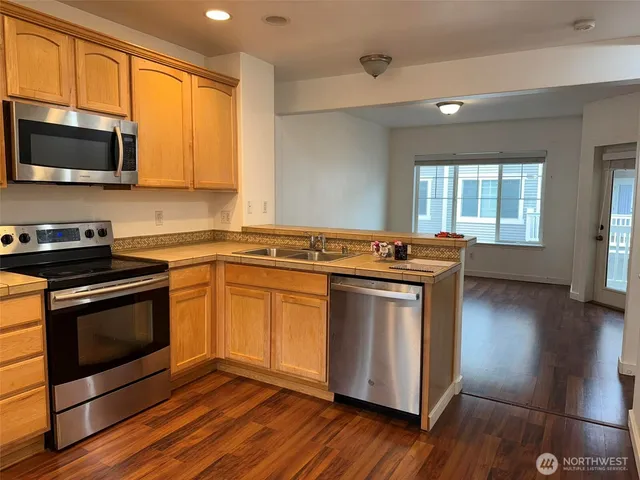 a kitchen with stainless steel appliances granite countertop a refrigerator a sink dishwasher a stove and a wooden floor next to a window