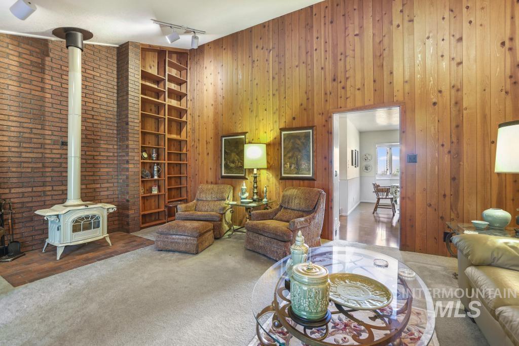 2018 Rancho Vista Drive Twin Falls, ID 83301 - Photo 18 of 50 Living area featuring a brick accent wall with a white wood-burning stove, built-in wood shelving, wood-paneled walls, and carpeted flooring
