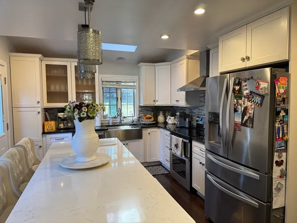 a kitchen with stainless steel appliances granite countertop a refrigerator a stove and white cabinets with wooden floors