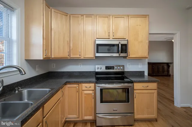 a kitchen with granite countertop wooden floors stainless steel appliances a sink and a window