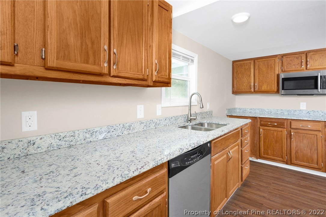 6129 Fisher Road Fayetteville, NC 28306 - Photo 11 of 31 a kitchen with granite countertop a sink dishwasher stove and cabinets with wooden floor