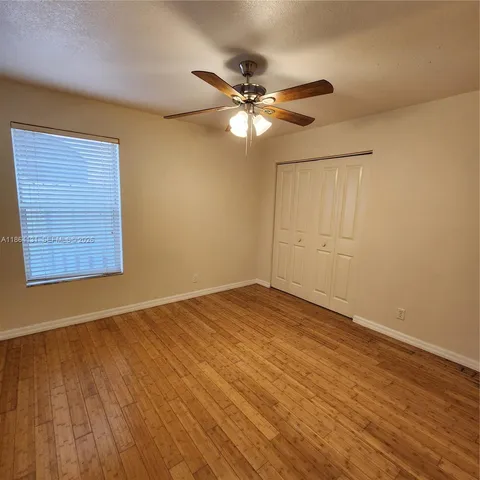 a view of an empty room with wooden floor and a ceiling fan