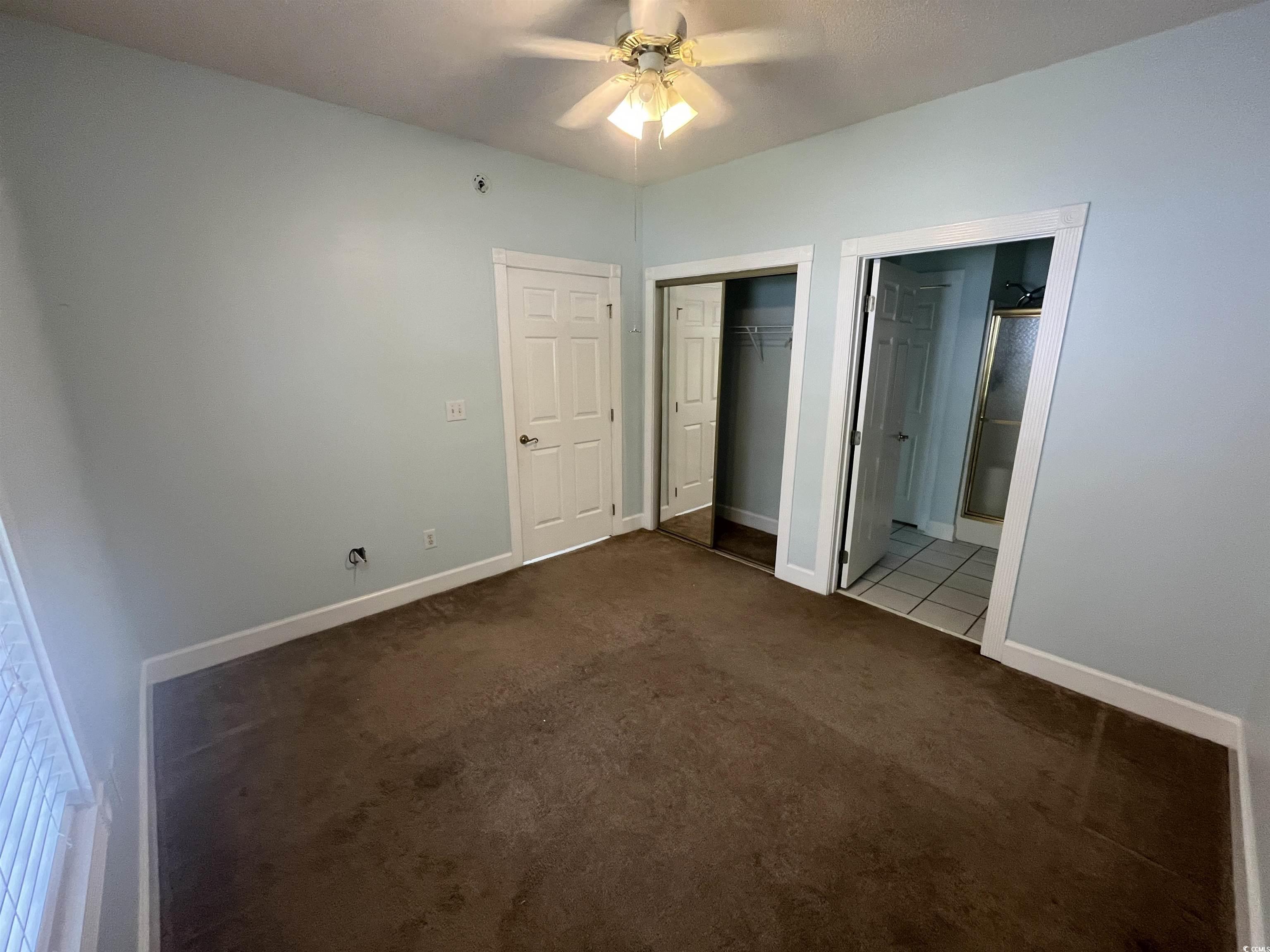 1514 Lanterns Rest Road, Unit 101 Myrtle Beach, SC 29579 - Photo 12 of 20 Unfurnished bedroom featuring dark carpet, a closet, ensuite bathroom, and a ceiling fan
