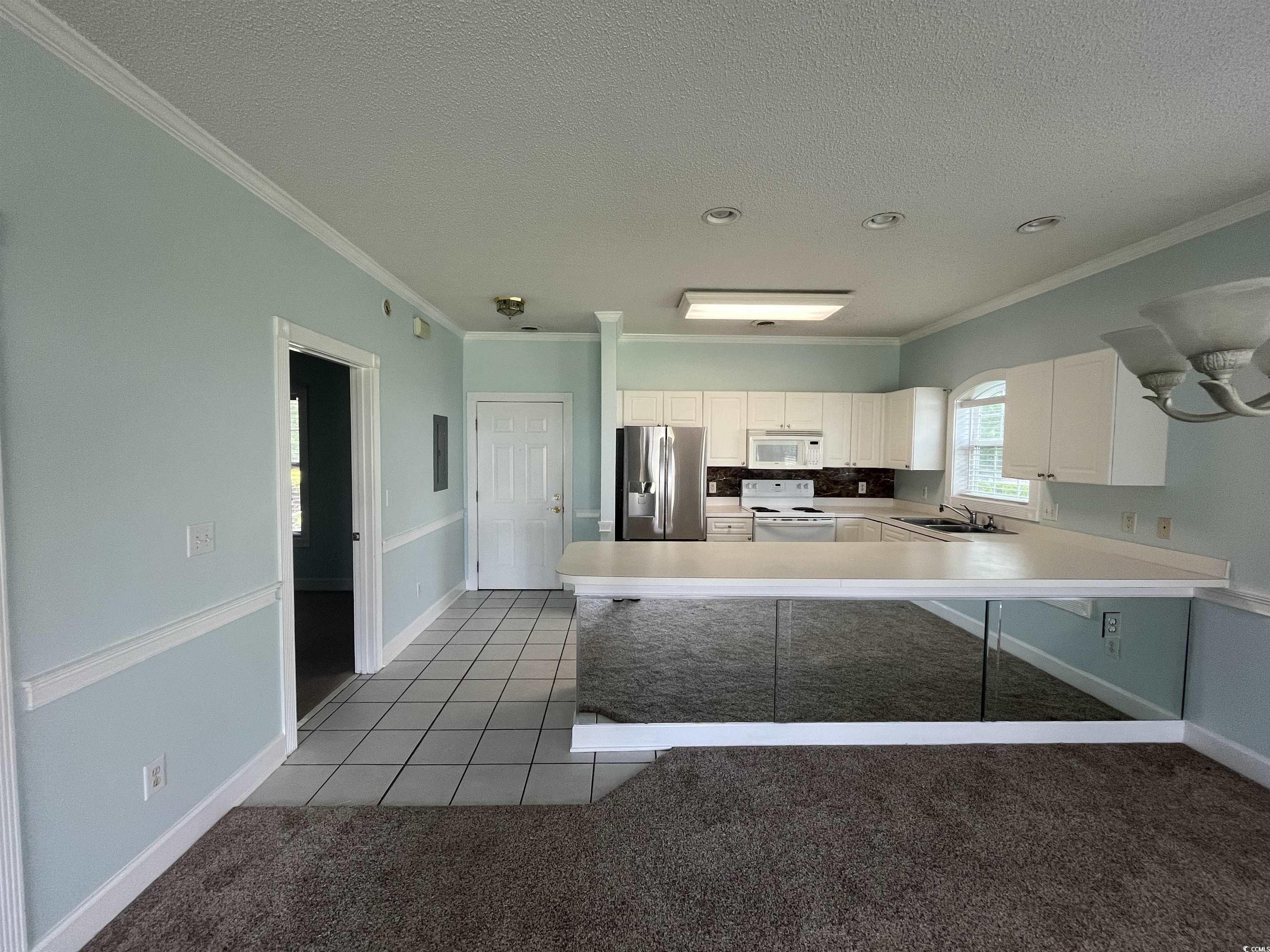 1514 Lanterns Rest Road, Unit 101 Myrtle Beach, SC 29579 - Photo 13 of 20 Kitchen featuring white appliances, crown molding, a textured ceiling, white cabinets, and a peninsula