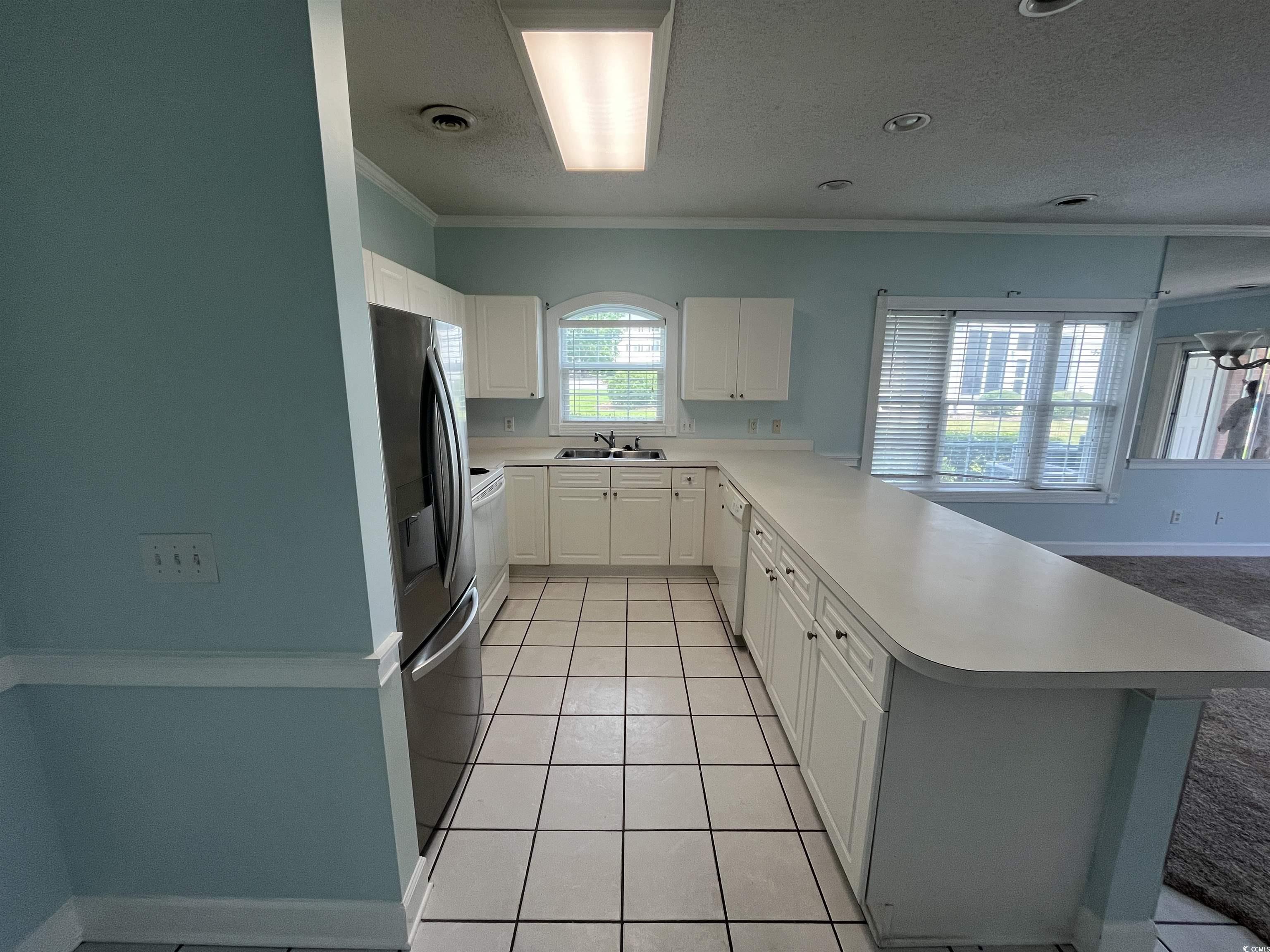 1514 Lanterns Rest Road, Unit 101 Myrtle Beach, SC 29579 - Photo 15 of 20 Kitchen featuring a peninsula, crown molding, stainless steel fridge, light countertops, and white cabinetry