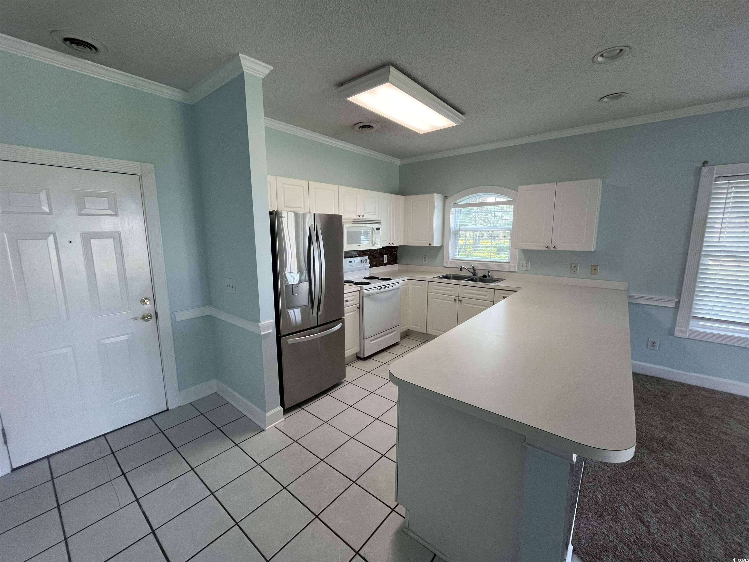 1514 Lanterns Rest Road, Unit 101 Myrtle Beach, SC 29579 - Photo 17 of 20 Kitchen featuring white appliances, a peninsula, white cabinetry, crown molding, and light countertops