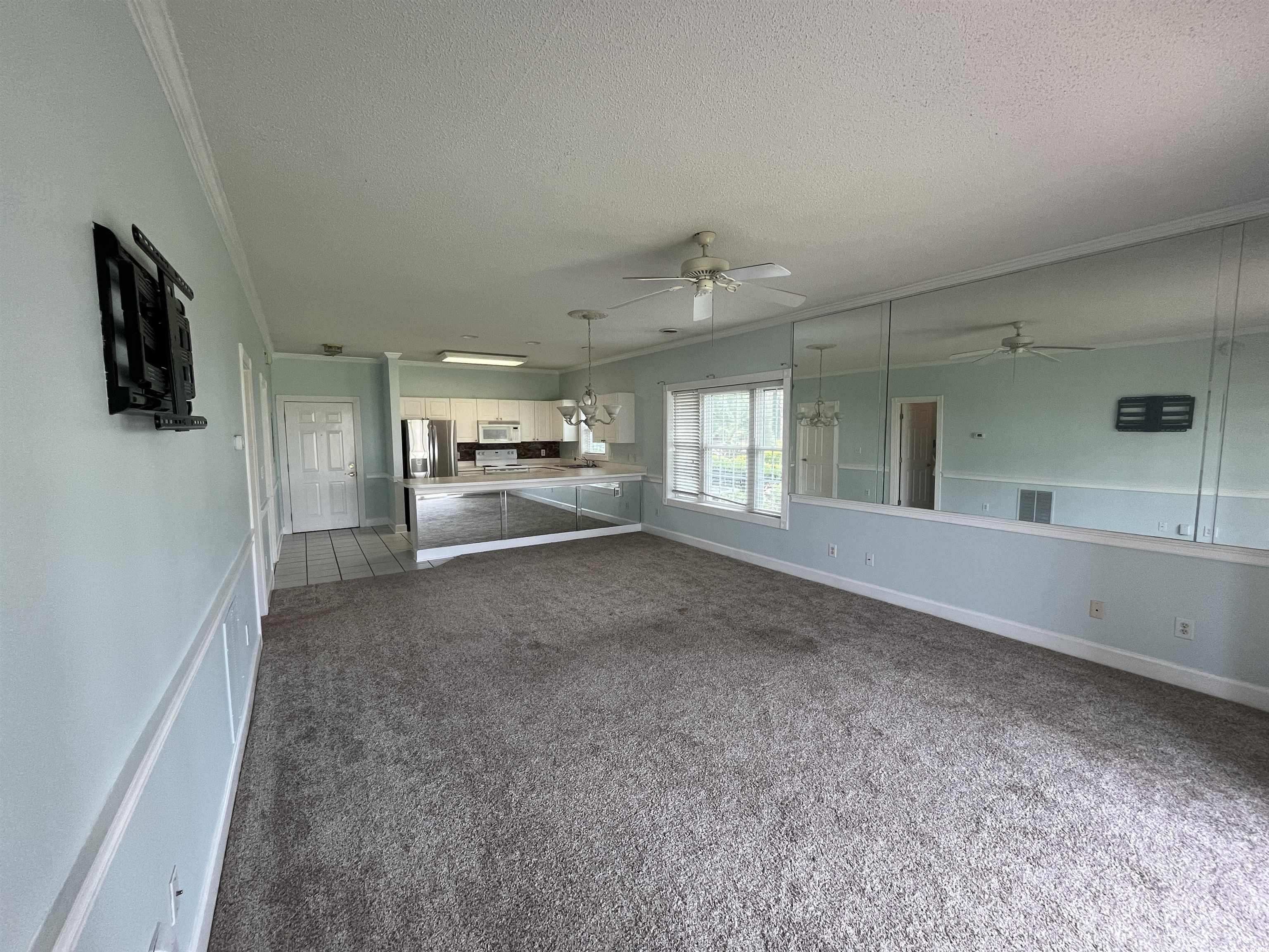 1514 Lanterns Rest Road, Unit 101 Myrtle Beach, SC 29579 - Photo 6 of 20 Unfurnished living room with a ceiling fan, dark colored carpet, a textured ceiling, and crown molding