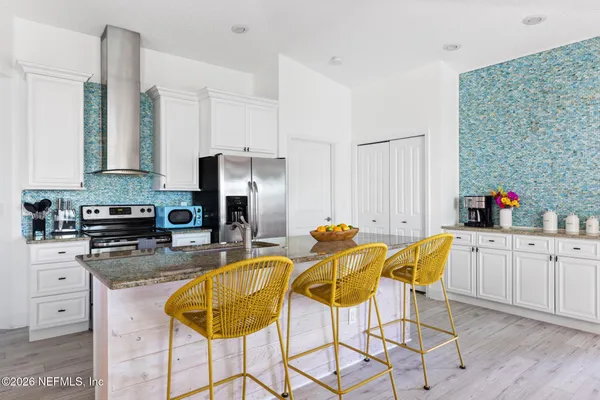 a kitchen with stainless steel appliances kitchen island granite countertop a dining table chairs and a refrigerator