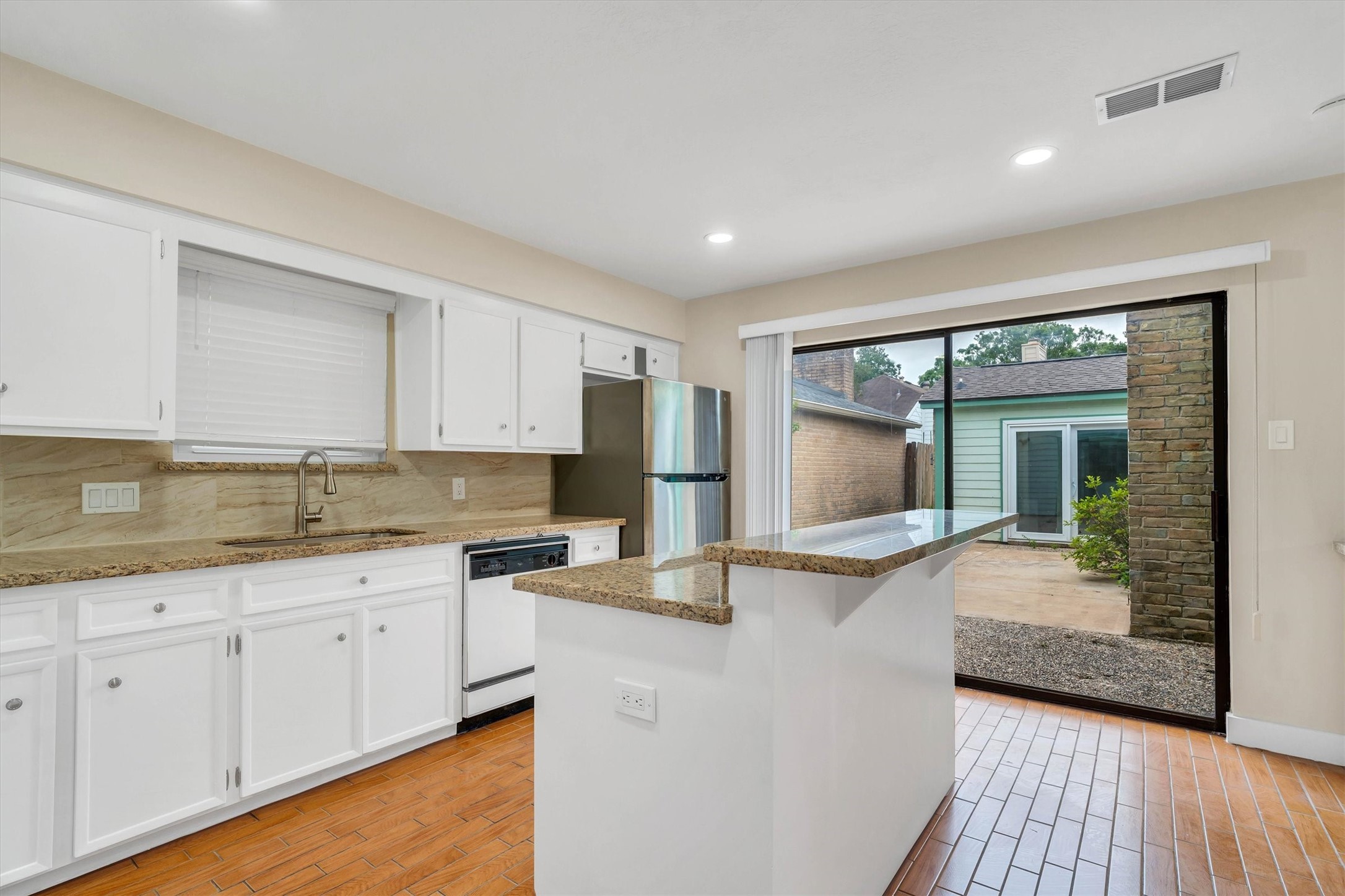 2163 Paso Rello Drive Houston, TX 77077 - Photo 15 of 45 Bright kitchen with white cabinets, granite countertops, and stainless steel appliances. Features a breakfast bar and large sliding glass doors opening to a patio, providing ample natural light.