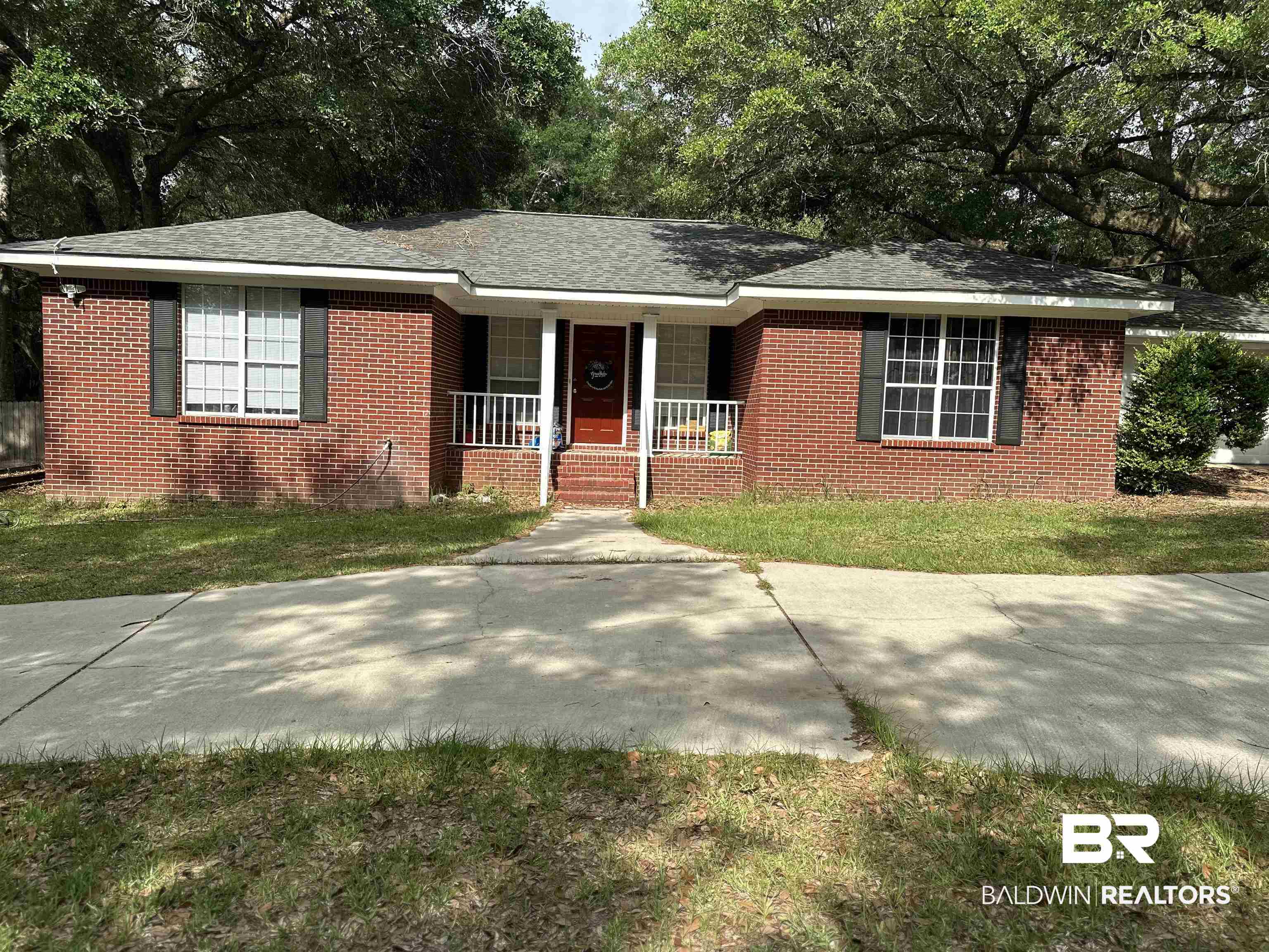 12602 McKee Road Irvington, AL 36544 - Photo 1 of 1 Brick exterior with dark shutters, a covered front porch, and a concrete driveway