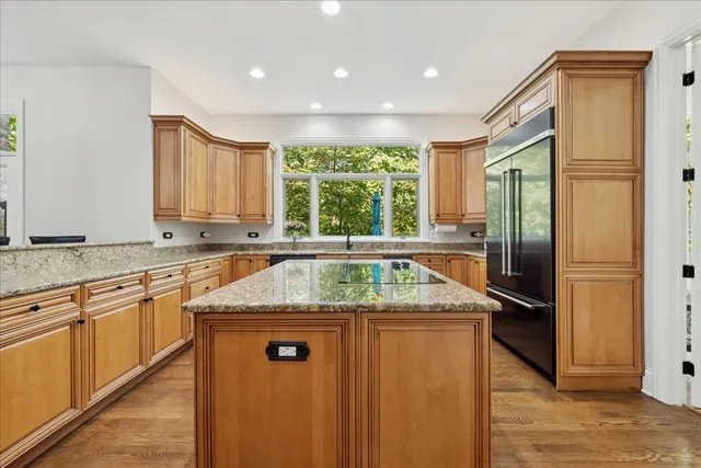 a kitchen with stainless steel appliances granite countertop a refrigerator a sink dishwasher a stove and a dining table with wooden floor