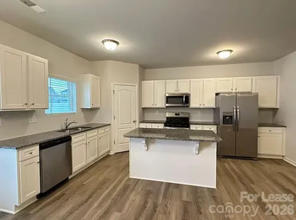 a kitchen with stainless steel appliances a microwave a stove a sink dishwasher a refrigerator and white cabinets with wooden floor