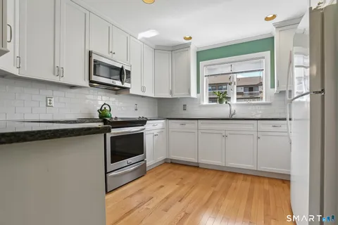 a kitchen with stainless steel appliances granite countertop white cabinets a sink a window and a counter space
