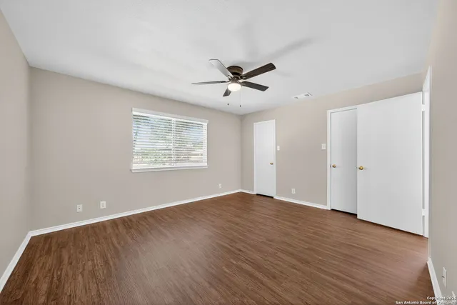 an empty room with wooden floor ceiling fan and windows