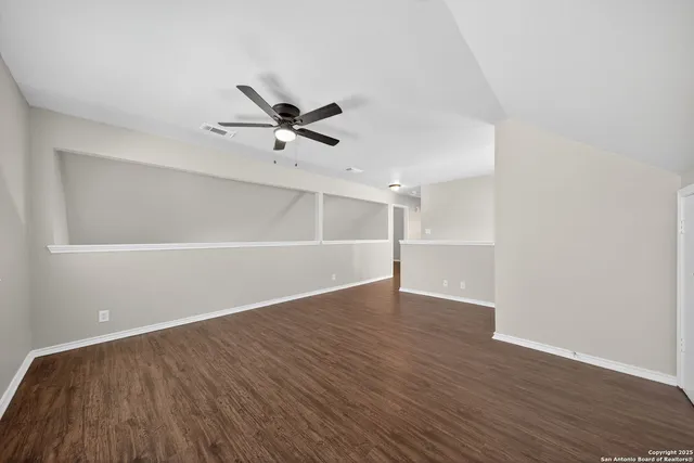 a view of an empty room with wooden floor and a ceiling fan